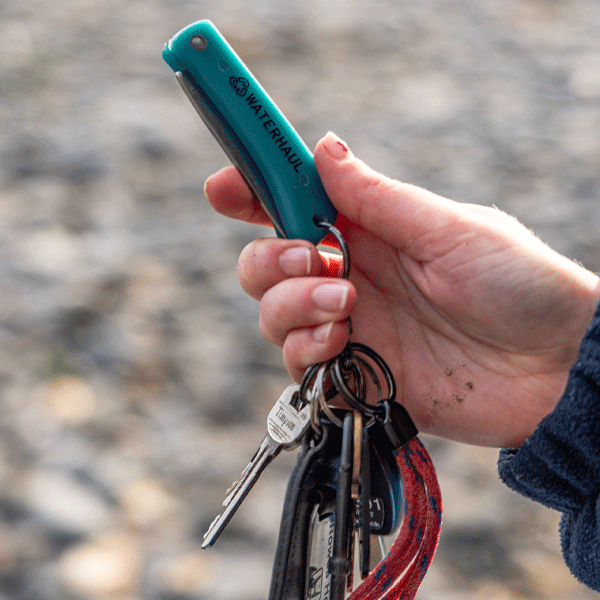 Hand holding green pocket knife attached to a set of keys
