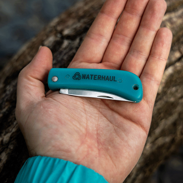 Hand holding small DC style pocket knife against wooden background