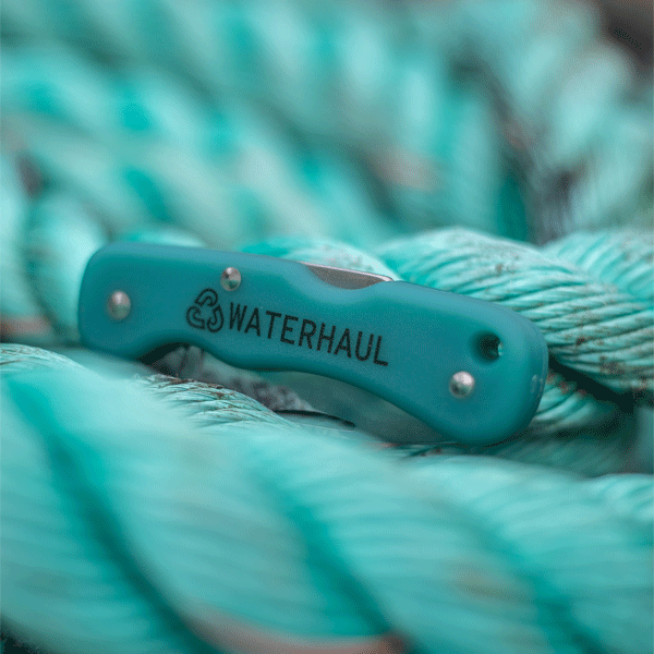 Blue pocket knife with 'WATERHAUL' branding on a background of green rope.
