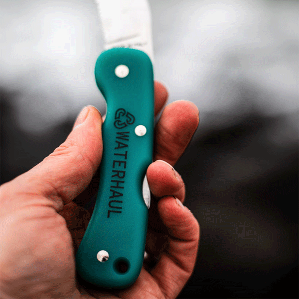 Hand holding a teal pocket knife with 'Waterhaul' branding against a blurred background