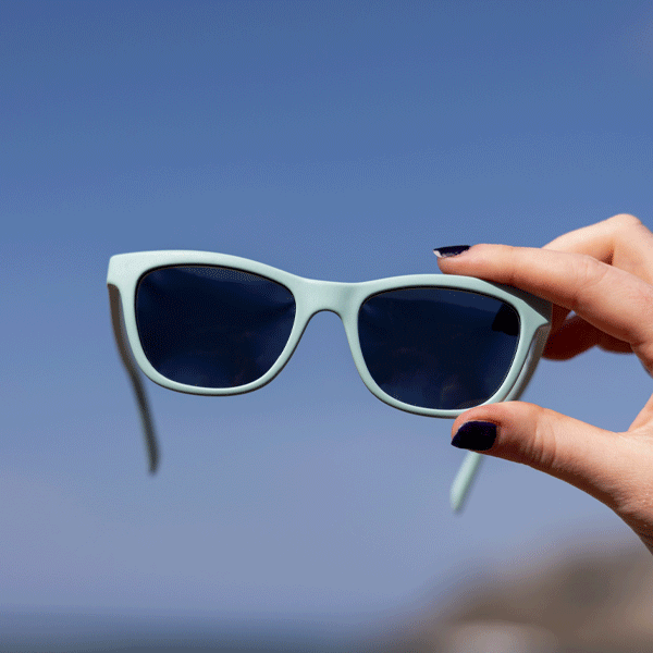 Hands holding aquamarine blue sunglasses against blue sky