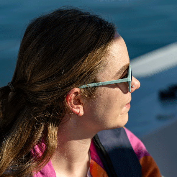 Woman on boat wearing light blue sunglasses and pink jumper