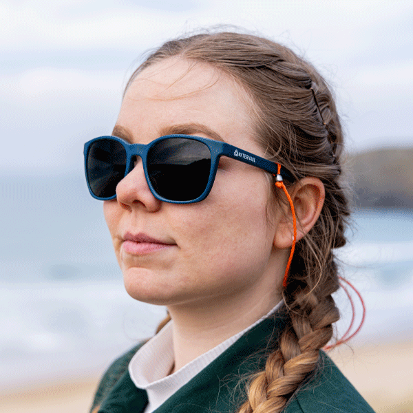 Woman wearing navy sunglasses with orange sunglasses strap in a coastal setting