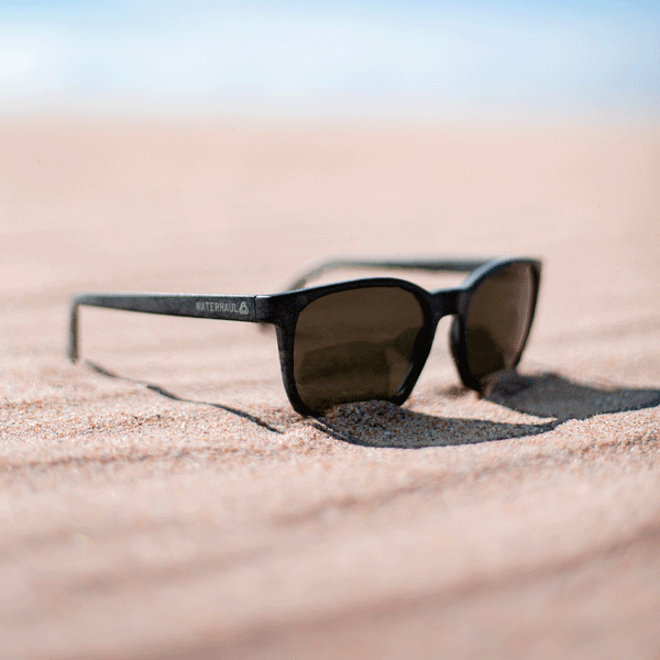 Black sunglasses with a dark lens on a sandy surface