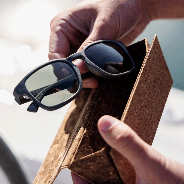 Person holding a pair of sunglasses with a cork case