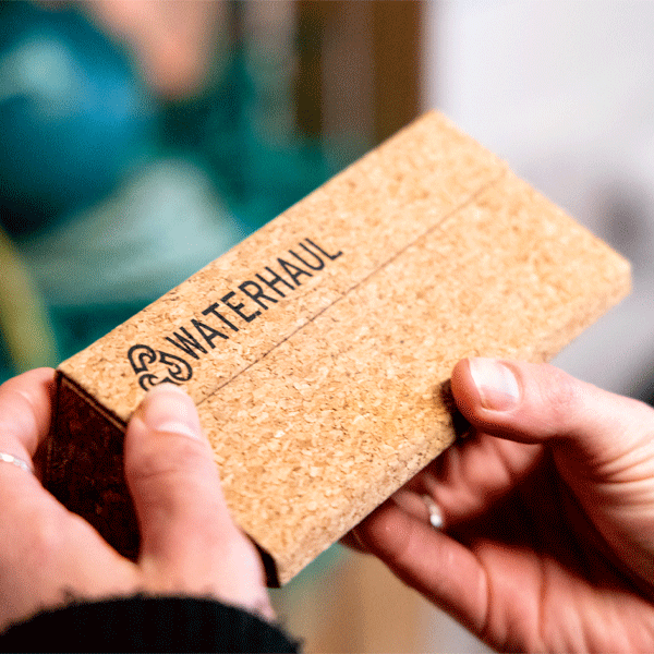Cork sunglasses case with 'WATERHAUL' branding held by hands against a blurred background