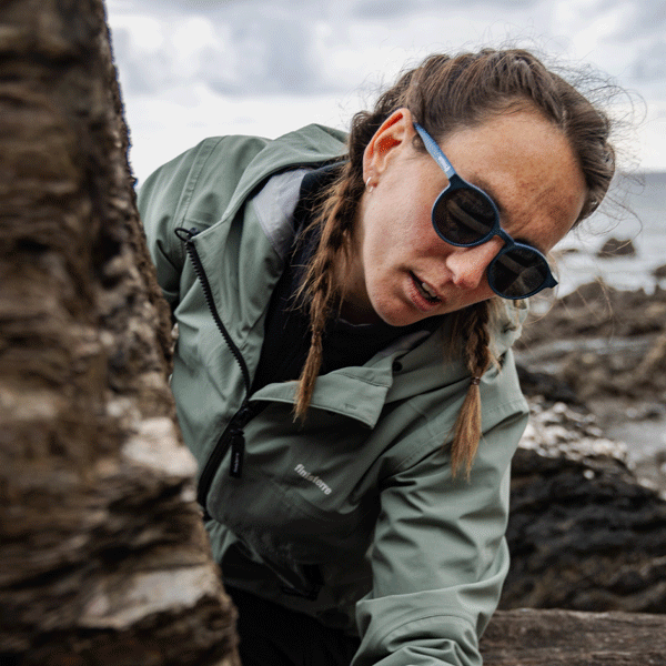 Person wearing a green jacket and round sunglasses in a rocky outdoor setting