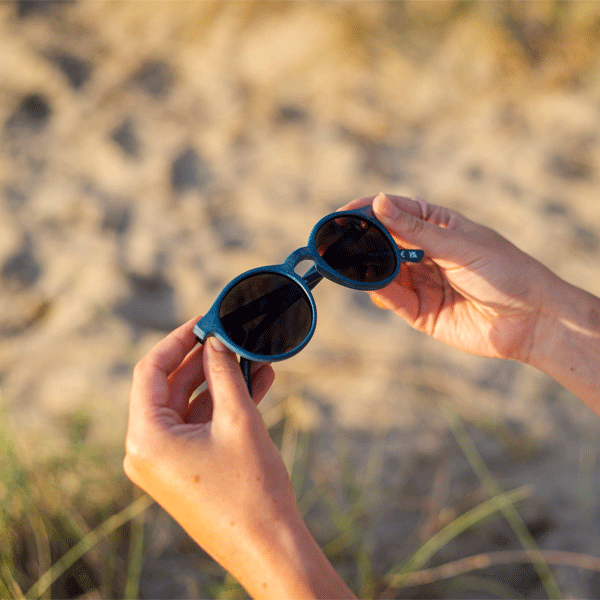 Person holding sunglasses with a blurred natural background