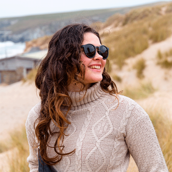 Woman wearing sunglasses and a beige jumper in a coastal setting