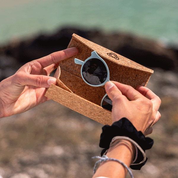 Cork sunglasses case with sunglasses held by hands against a blurred natural background