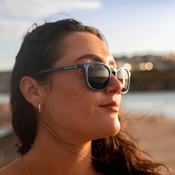 Woman wearing navy blue sunglasses on a beach at sunset