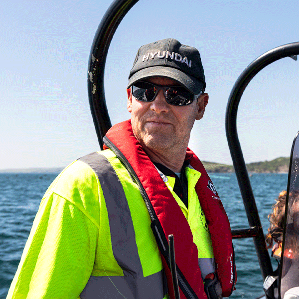 Man wearing a cap and sunglasses in sailing gear on a boat with an ocean background