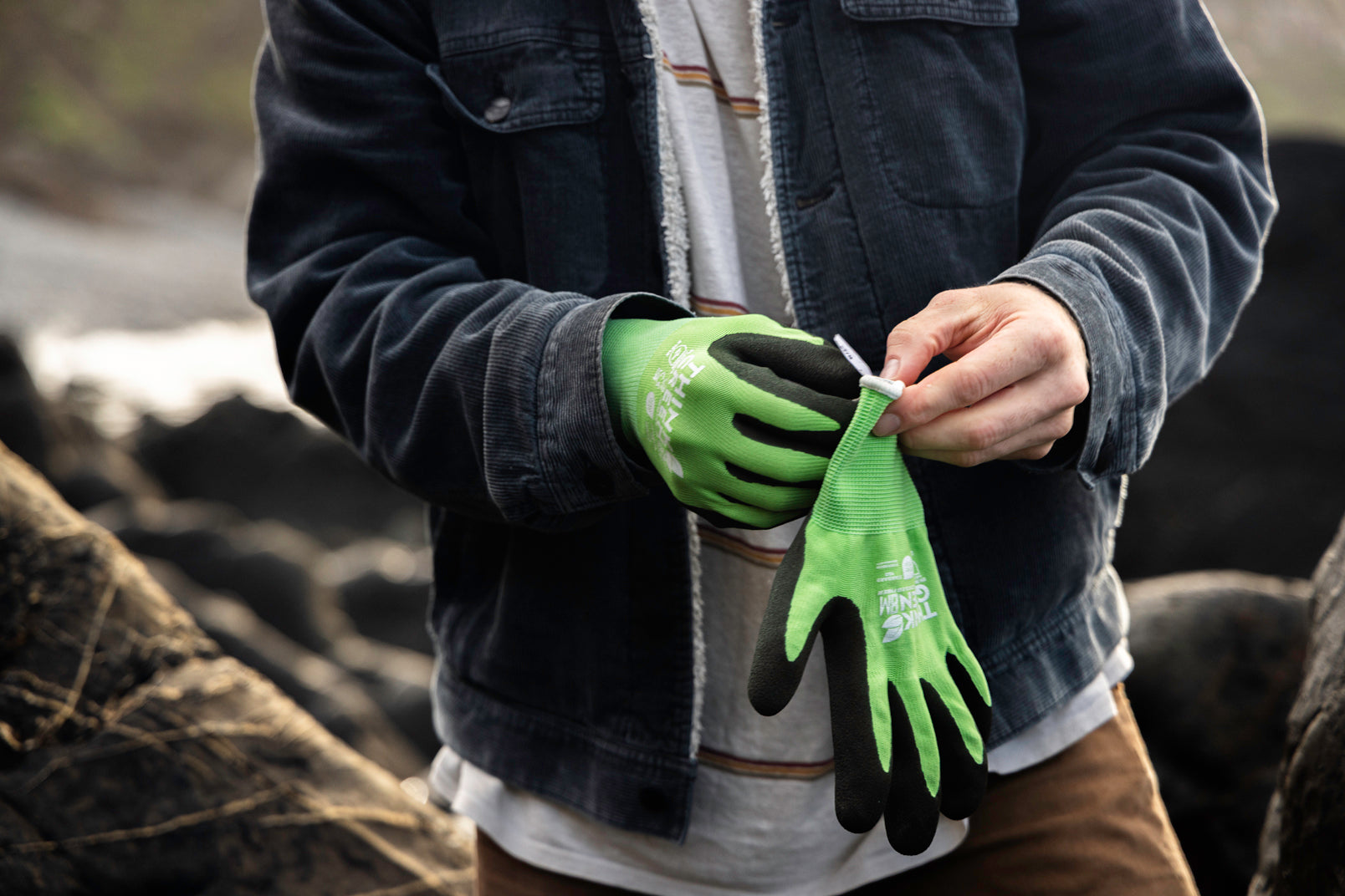 Person putting on green gardening gloves for a beach clean in a rocky setting.
