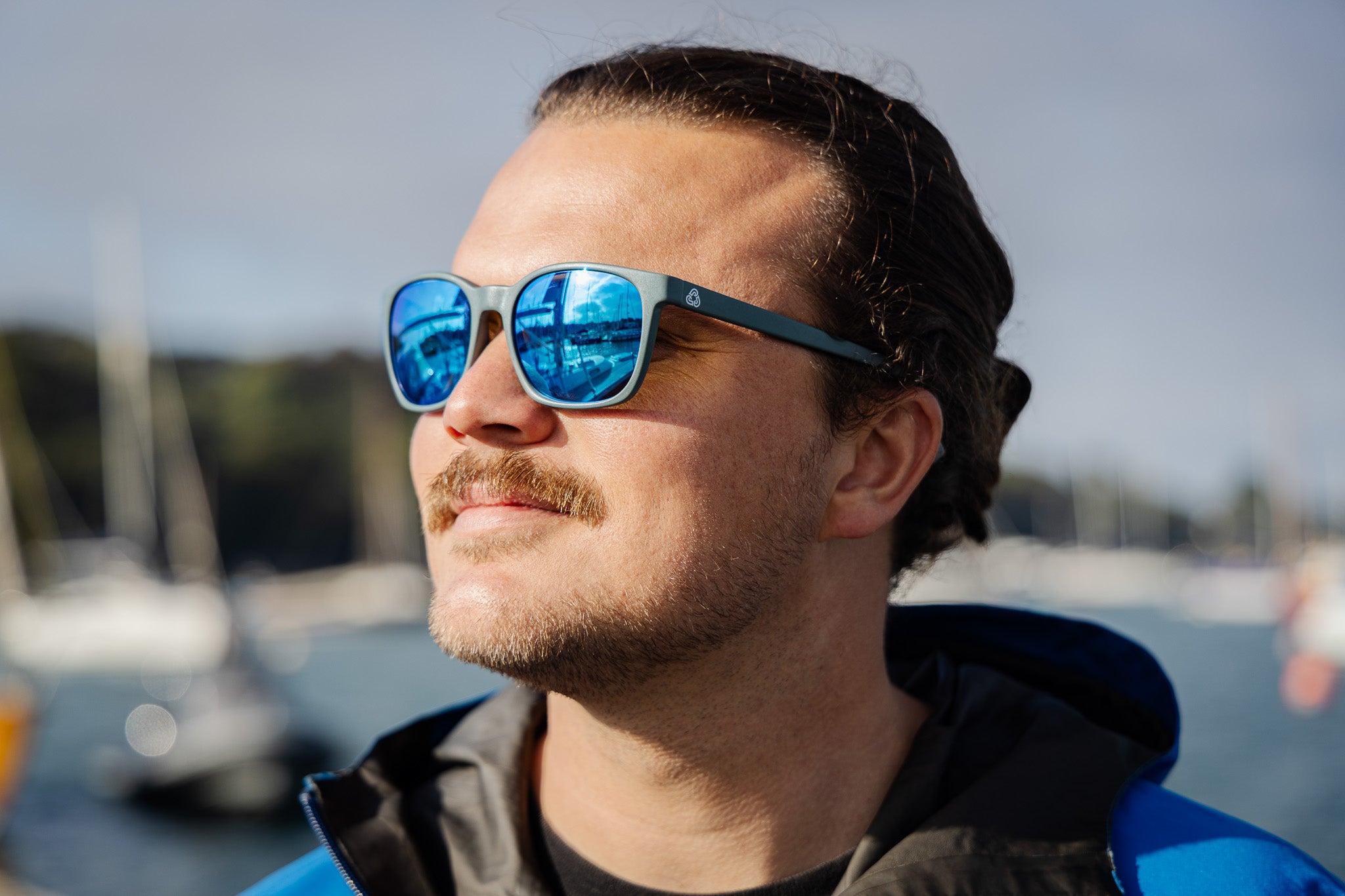 Man wearing sunglasses with blue lenses with a blurred background of water and boats
